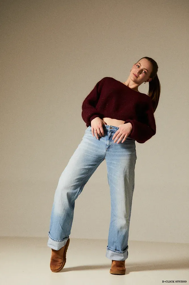 Pauline en pull bordeaux et jean, pose studio décontractée.