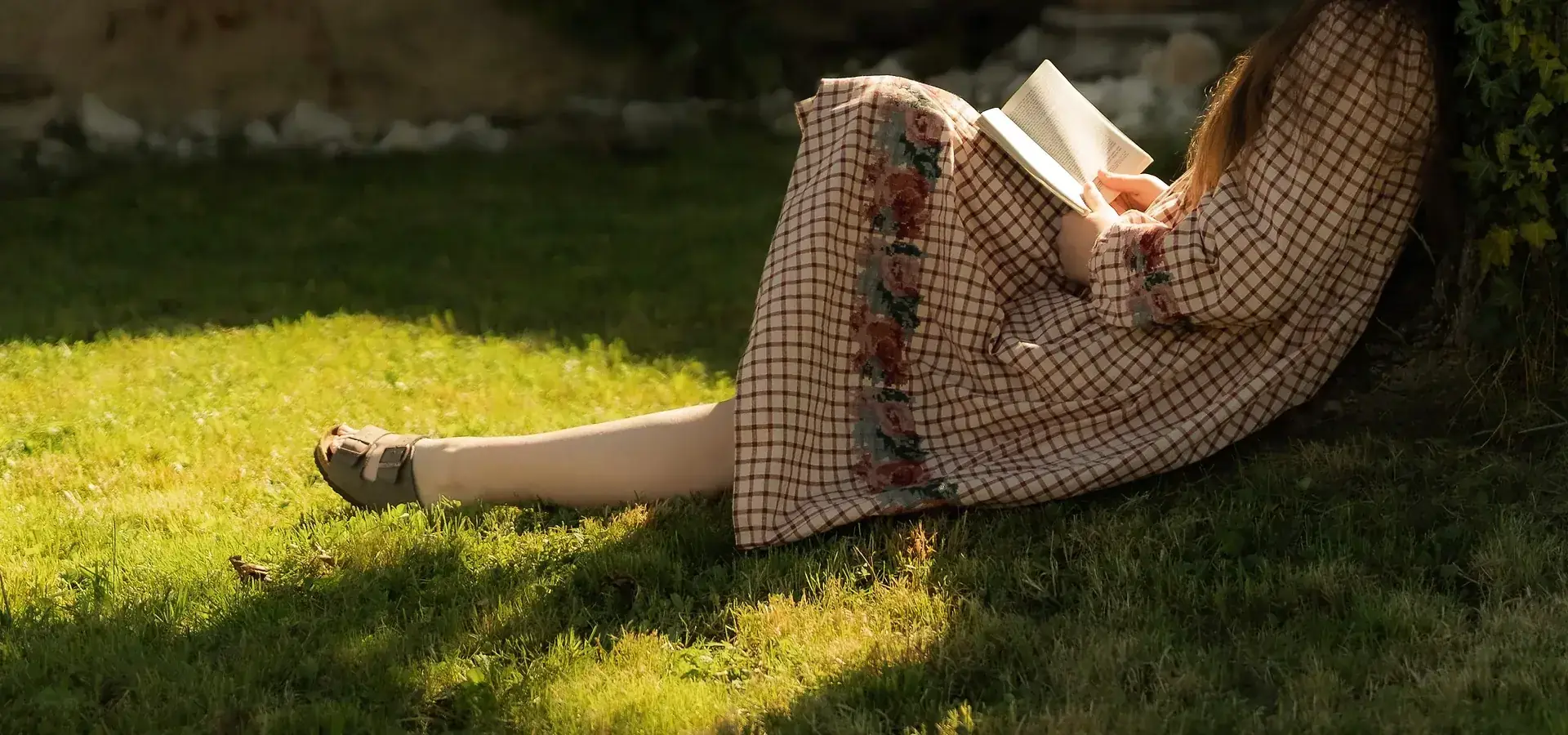 Allongée dans l'herbe, un livre à la main, chemise à carreaux.