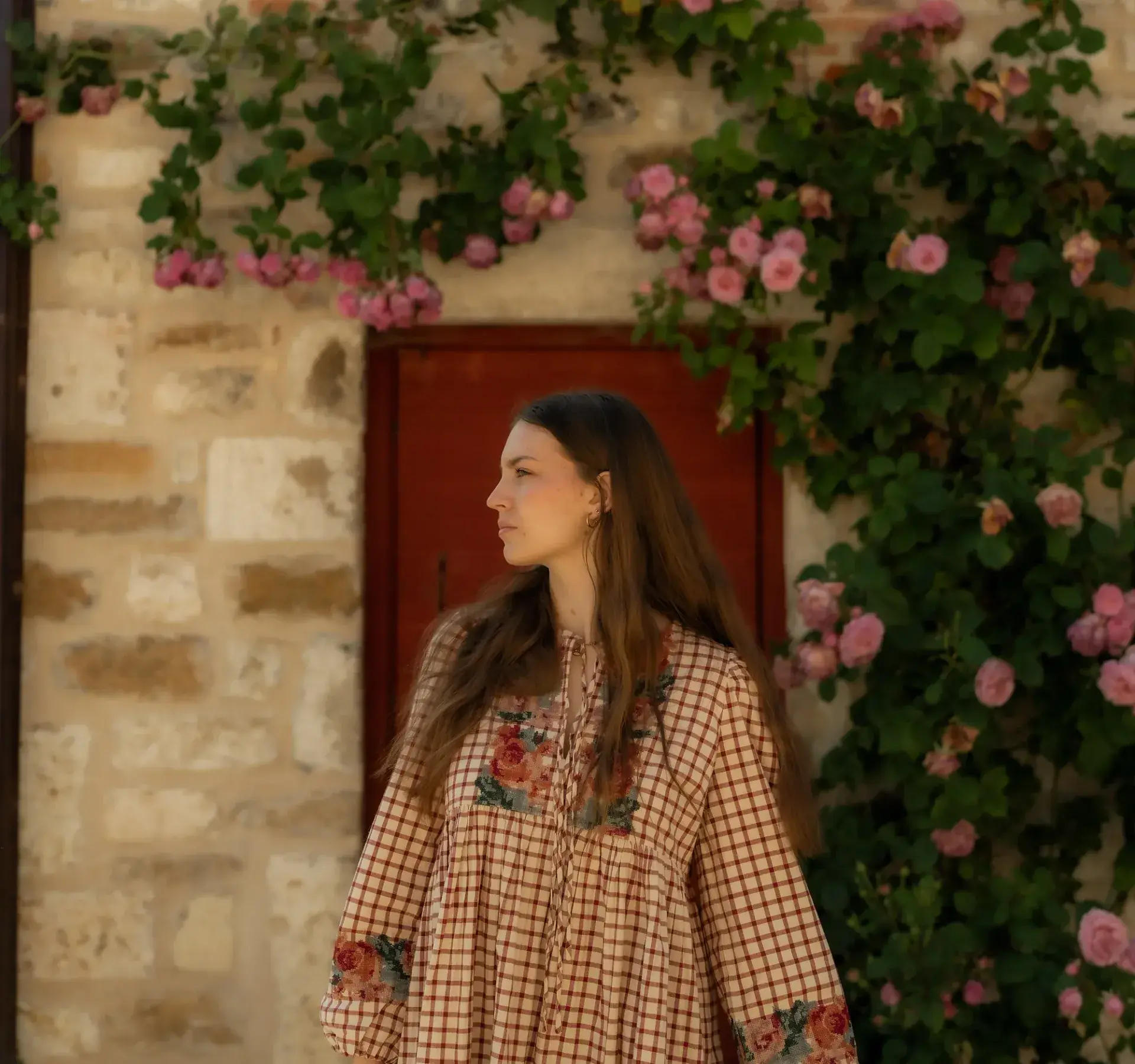 Pauline Bejeannin de profil devant un mur de pierre couvert de roses grimpantes, lumière douce.